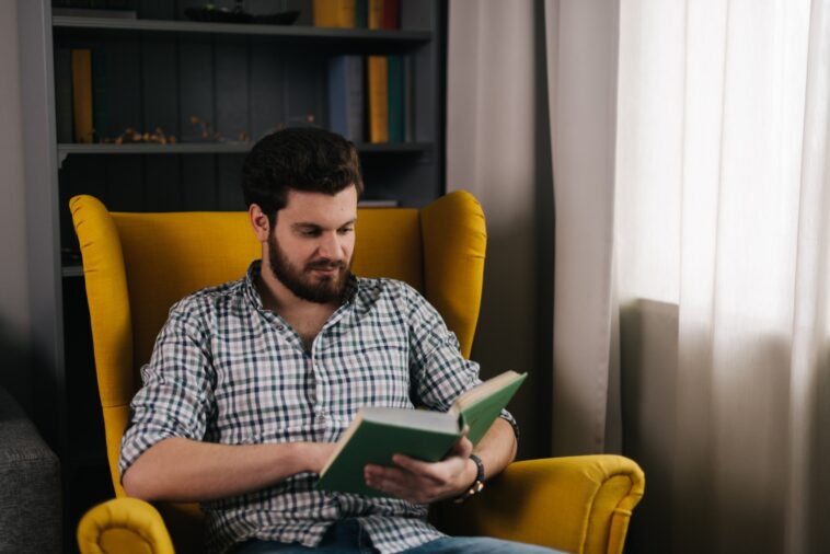 man sitting in a yellow chair reading a book